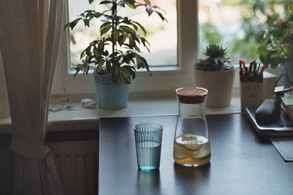 a glass of water next to a small carafe on a desk with plants