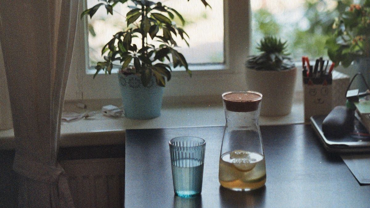 a glass of water next to a small carafe on a desk with plants