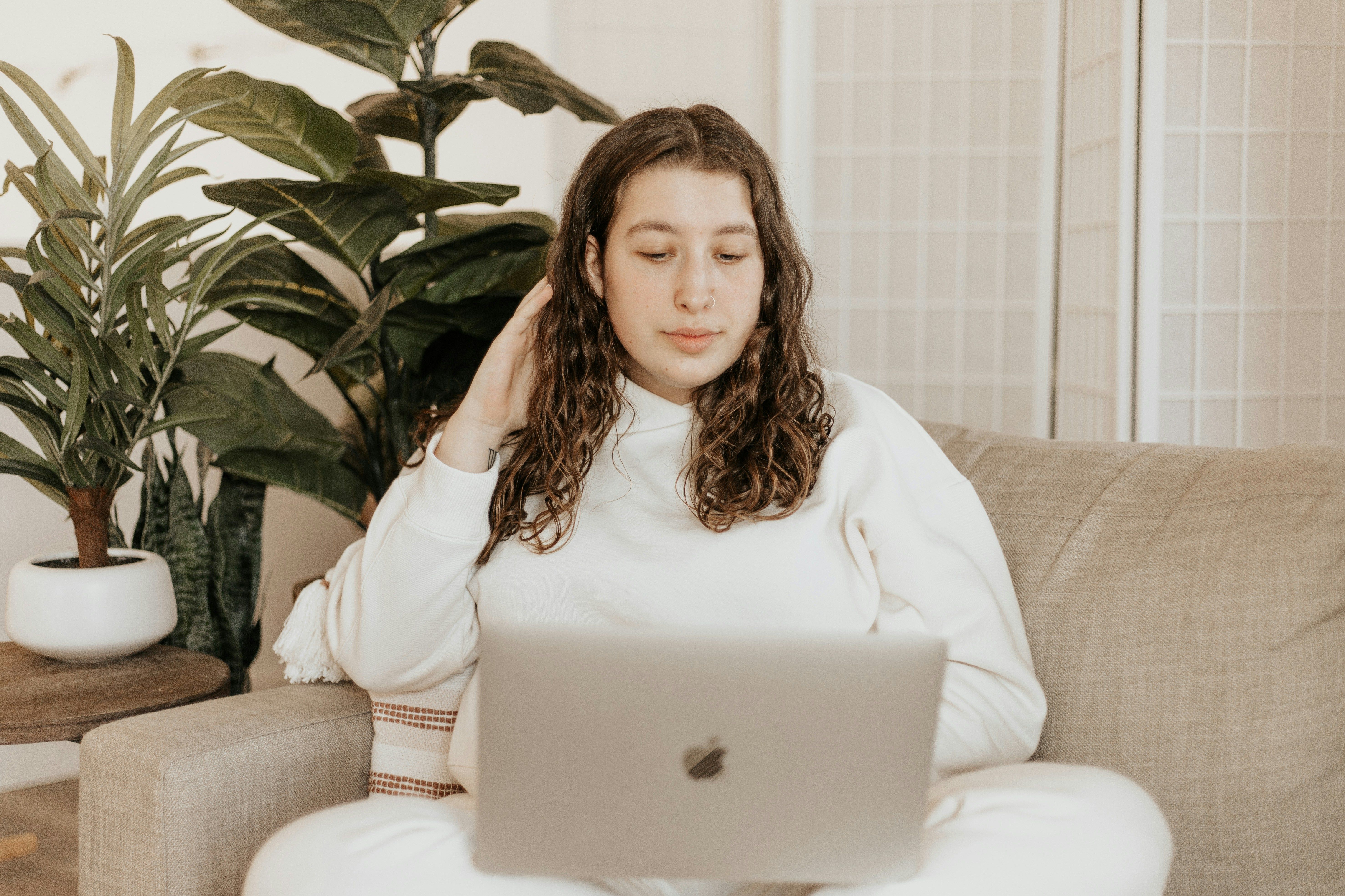 woman in white long sleeve shirt sitting on white couch with laptop