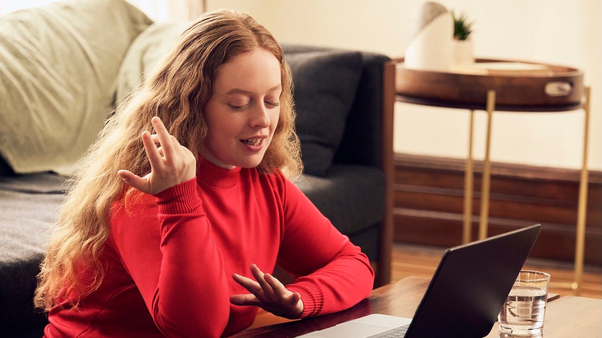 a young woman in a red sweater sitting in her living room talking to a therapist in a free online consultation