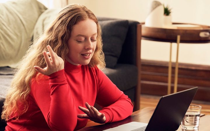 a young woman in a red sweater sitting in her living room talking to a therapist in a free online consultation