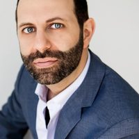 Dr. David Sitt, photographed sitting in a studio wearing a dark blue suit that matches his eyes.