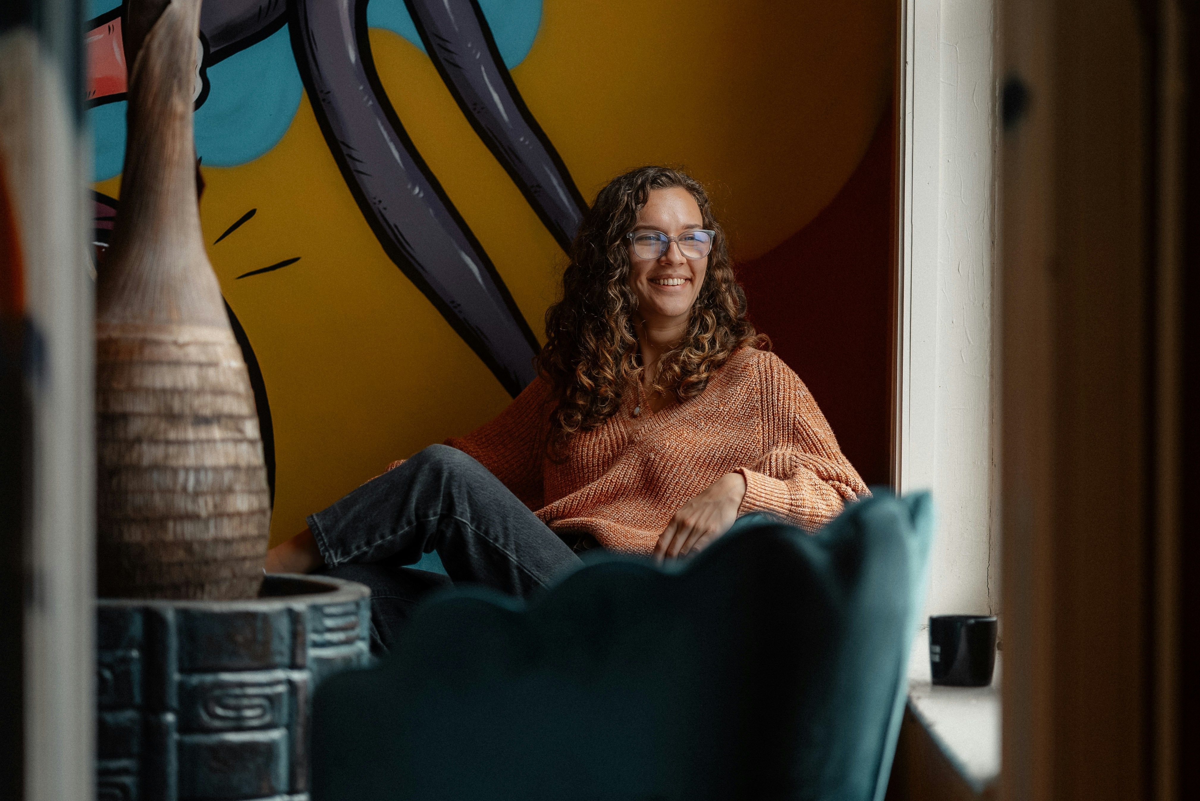 A smiling woman sitting in a chair in front of a painting