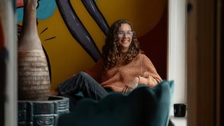A smiling woman sitting in a chair in front of a painting