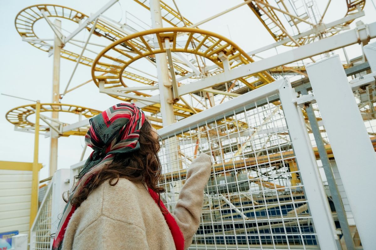 A woman in a colorful head scarf pointing at a rollercoaster