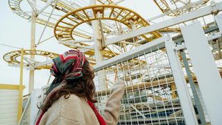 A woman in a colorful head scarf pointing at a rollercoaster