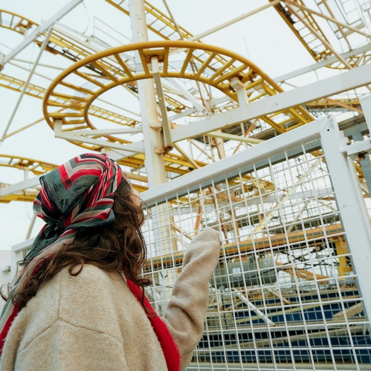 A woman in a colorful head scarf pointing at a rollercoaster
