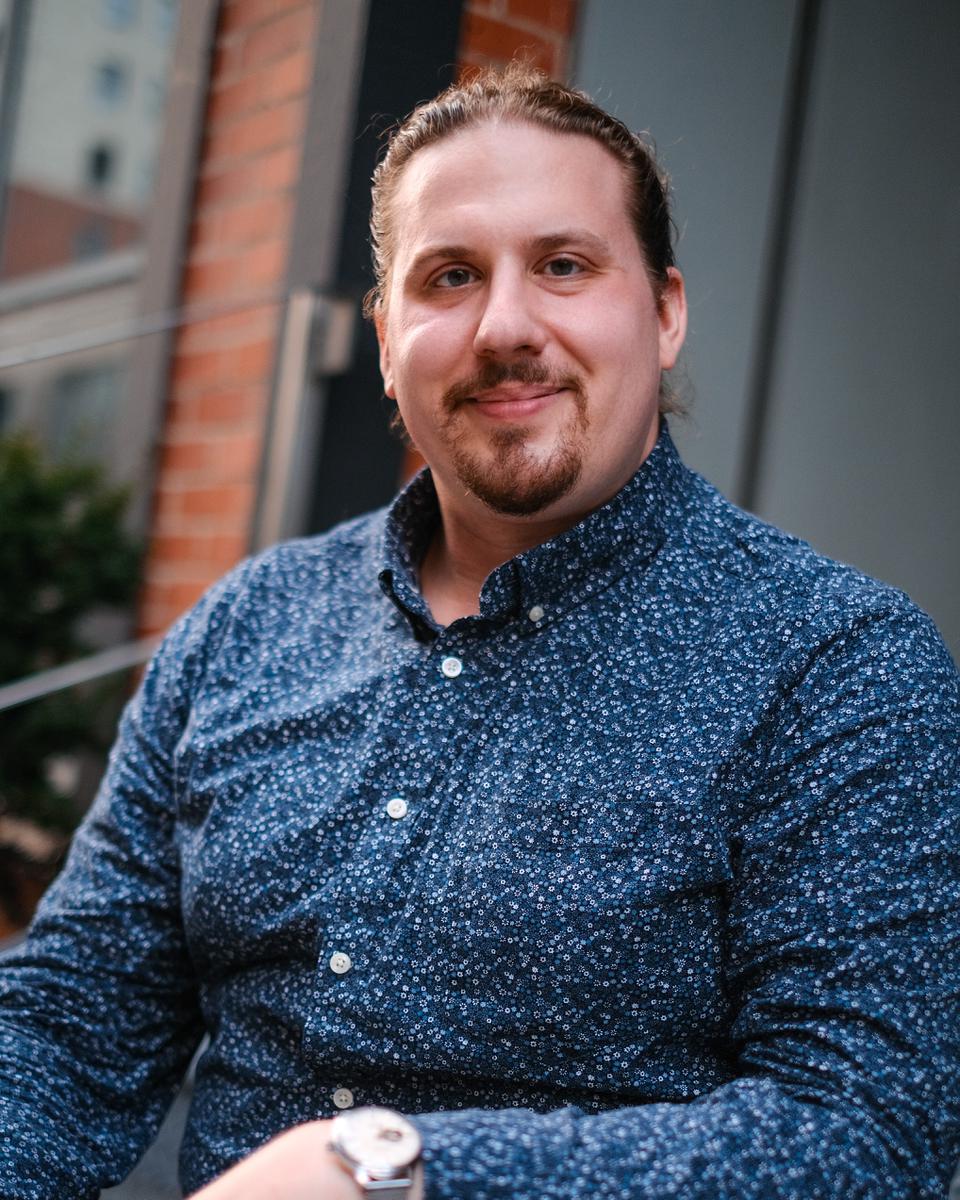 Paul, an Alma therapist, smiles warmly from a front stoop wearing a floral blue shirt.
