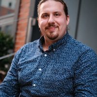 Paul, an Alma therapist, smiles warmly from a front stoop wearing a floral blue shirt.