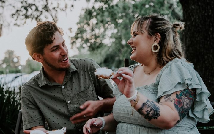 A photograph of two friends who seem to be blissfully disengaged from thinking about food, centered on a snack held in one hand.