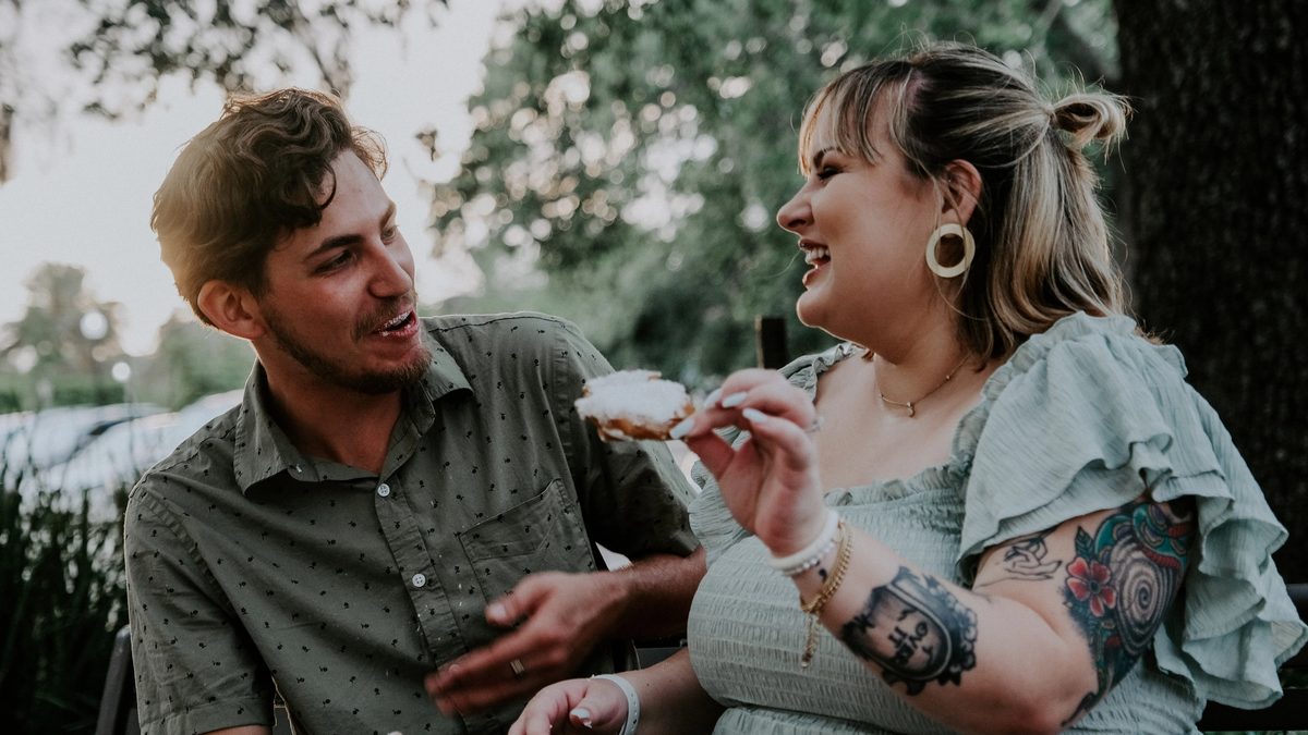 A photograph of two friends who seem to be blissfully disengaged from thinking about food, centered on a snack held in one hand.