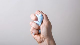 A light-skinned hand squeezing some kind of blue stress ball or putty.