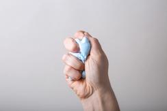 A light-skinned hand squeezing some kind of blue stress ball or putty.