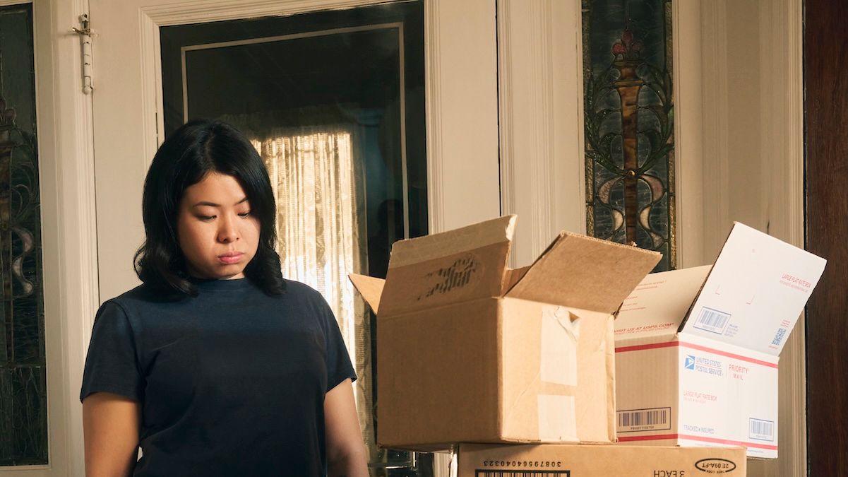A woman stands staring at boxes and mail piled up just inside her front door