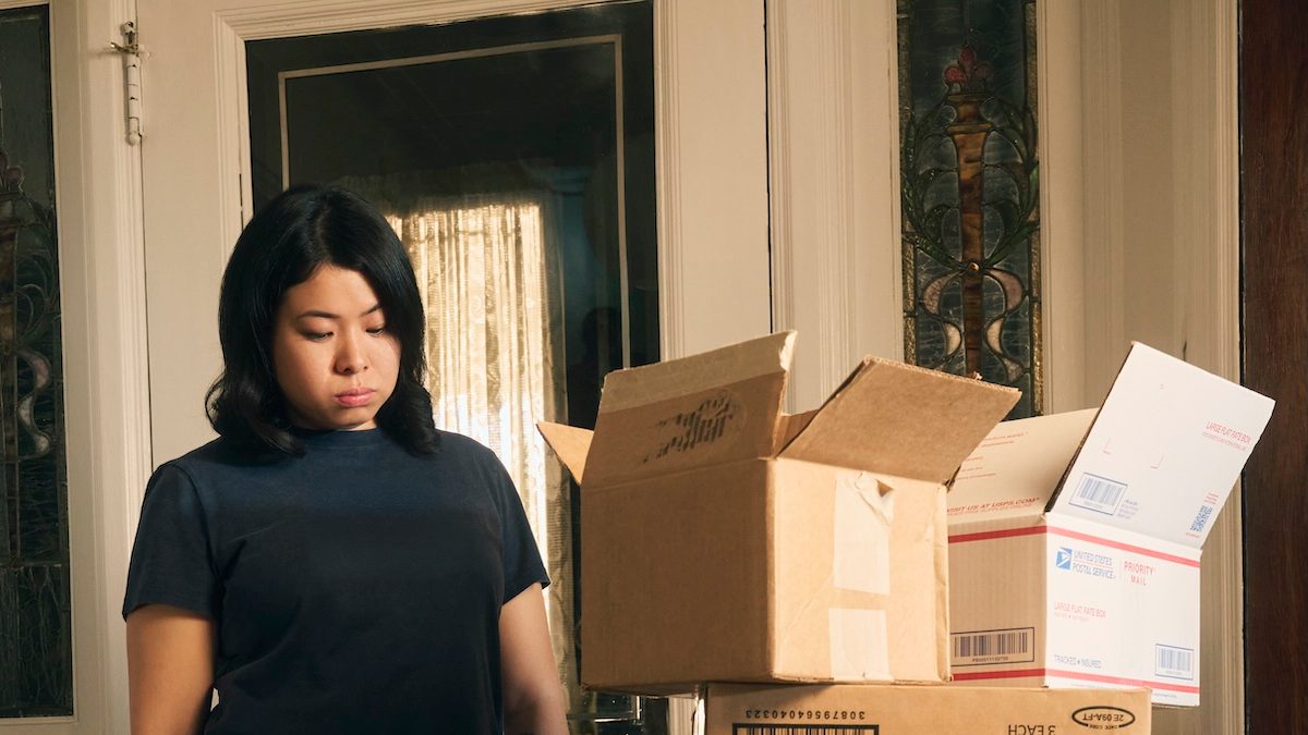 A woman stands staring at boxes and mail piled up just inside her front door