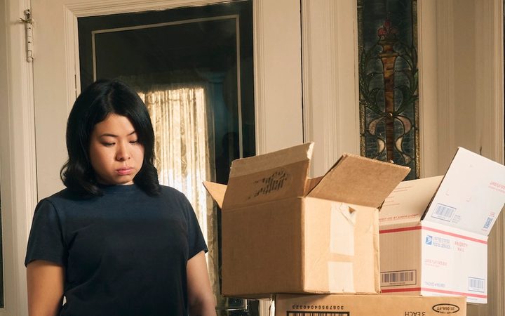 A woman stands staring at boxes and mail piled up just inside her front door