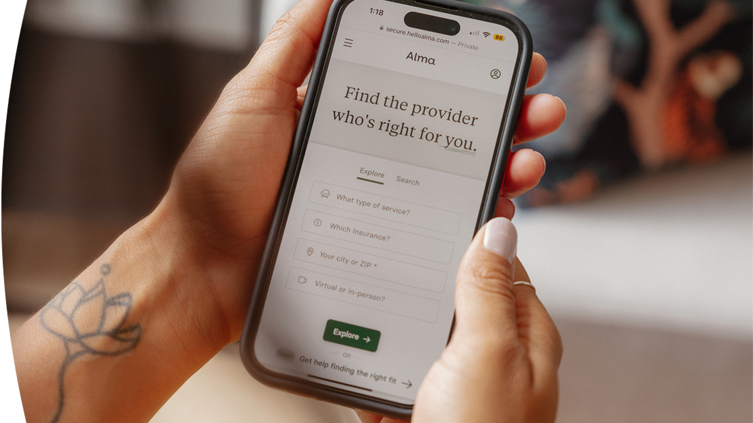 Person holding a smartphone with the Alma website open, showing a provider search tool to find the right therapist based on service, insurance, and location.