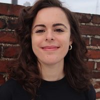 A photo of therapist and writer Elise Mendelsohn LMSW taken in Brooklyn, NY, in front of a brick wall and blue-gray sky