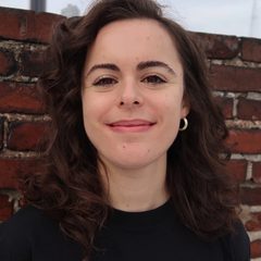 A photo of therapist and writer Elise Mendelsohn LMSW taken in Brooklyn, NY, in front of a brick wall and blue-gray sky