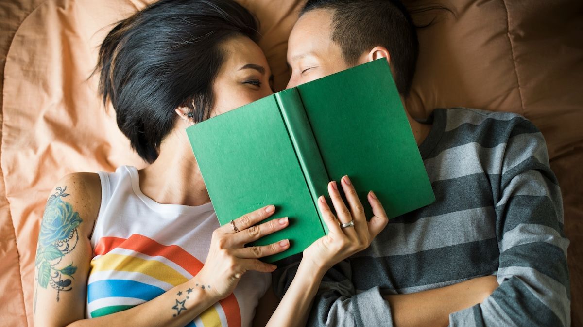 A couple is snuggling in bed with a book
