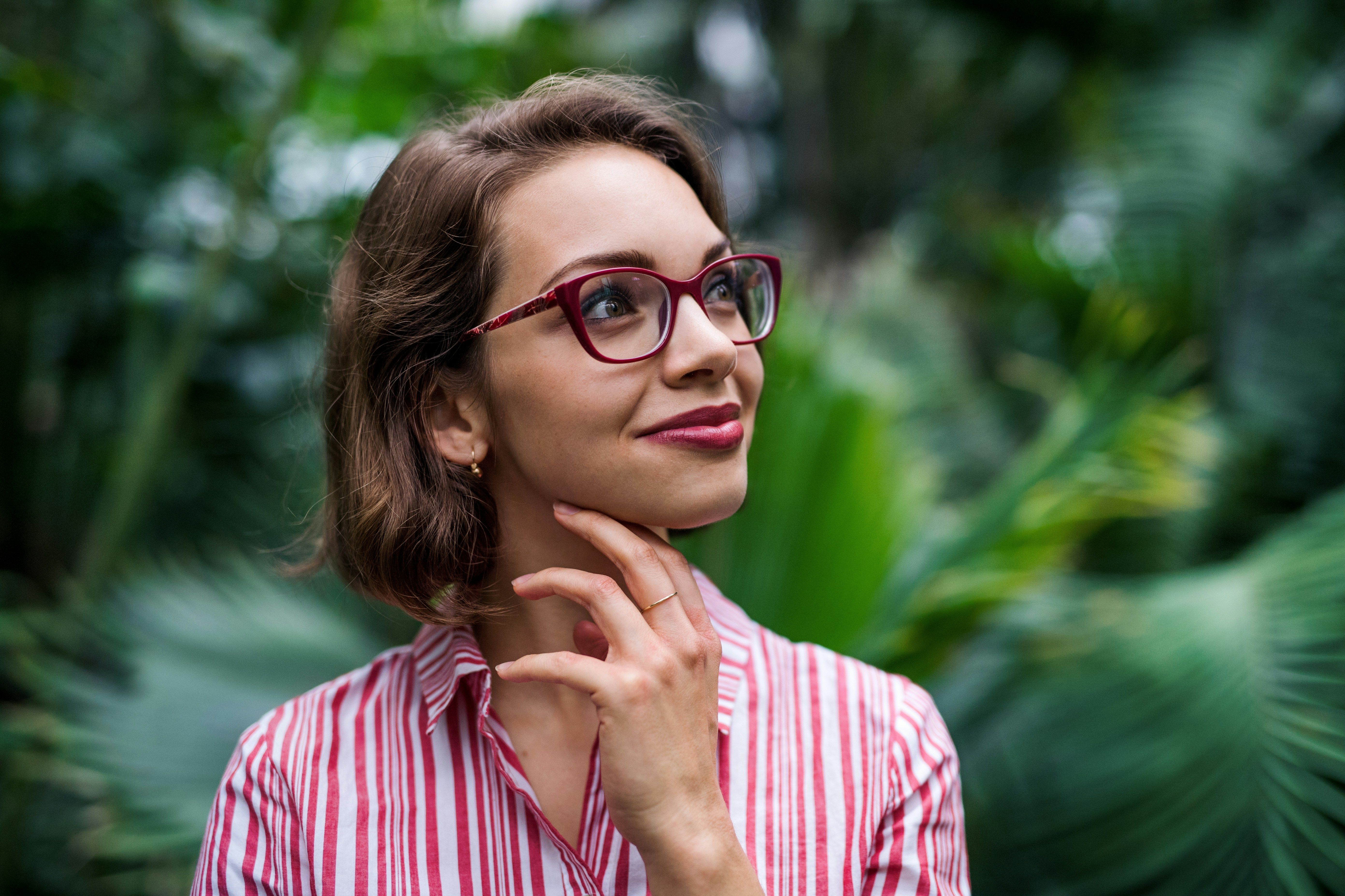 Woman with glasses smiling with a tropical forest background behind her