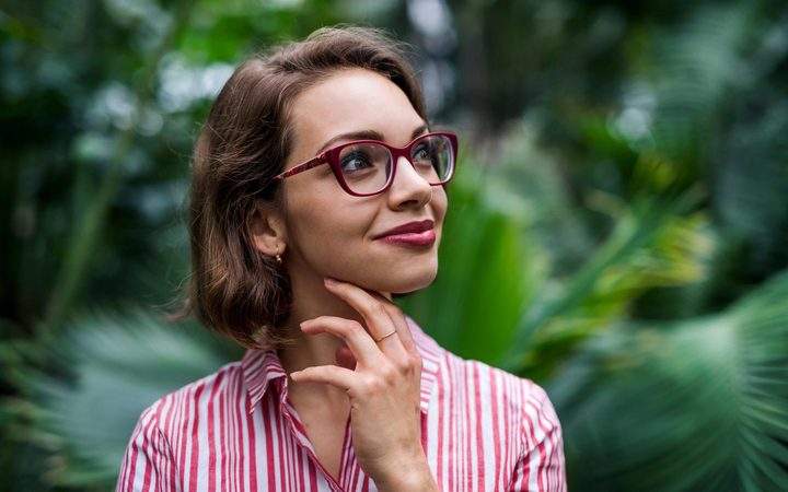 Woman with glasses smiling with a tropical forest background behind her