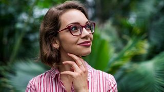 Woman with glasses smiling with a tropical forest background behind her