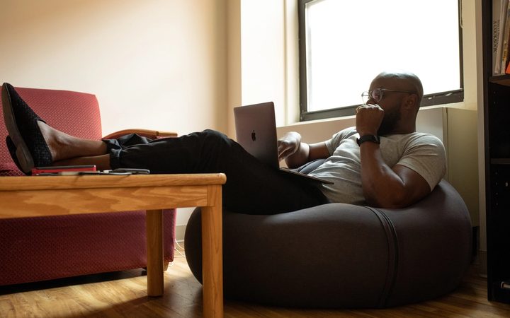 Person sitting in a bean bag chair with legs resting on a table while looking contemplatively at a laptop