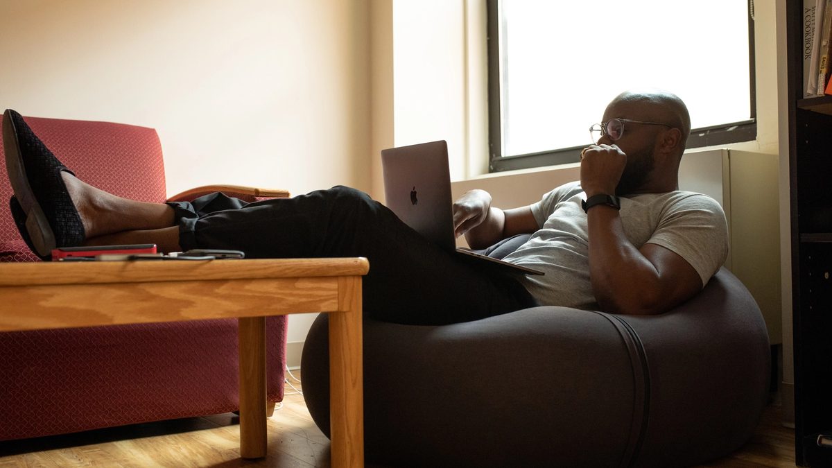Person sitting in a bean bag chair with legs resting on a table while looking contemplatively at a laptop