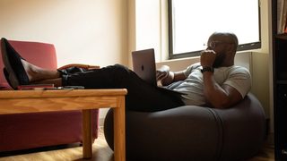 Person sitting in a bean bag chair with legs resting on a table while looking contemplatively at a laptop