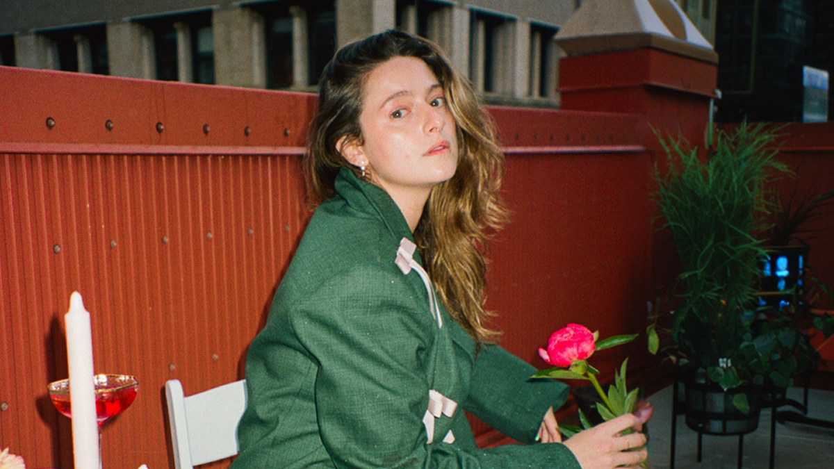 author Haley Jakobson sits on a rooftop at night holding a red rose