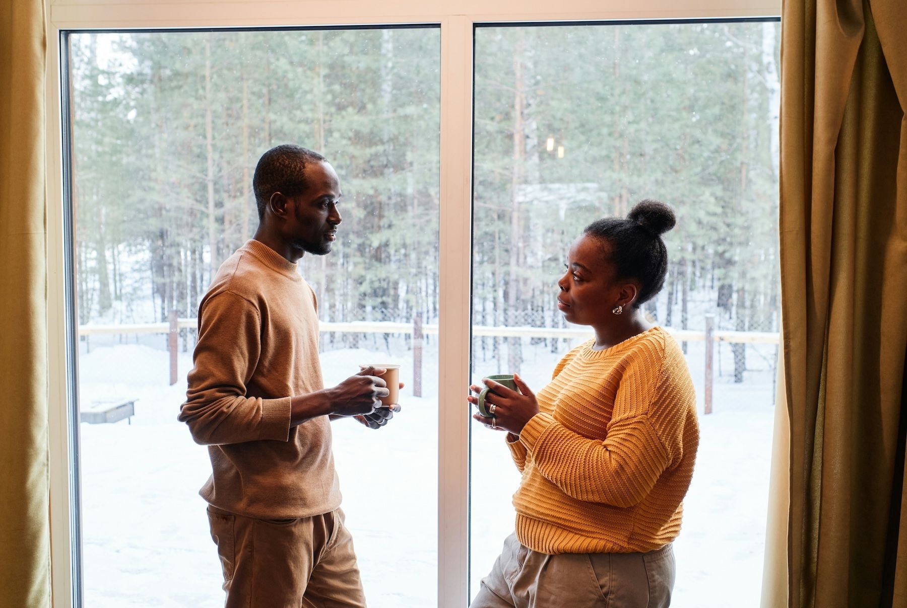 A couple stands facing each other in front of a glass sliding door having an in-depth conversation.