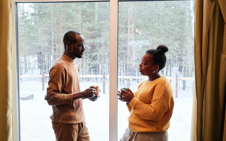 A couple stands facing each other in front of a glass sliding door having an in-depth conversation.