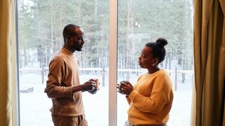 A couple stands facing each other in front of a glass sliding door having an in-depth conversation.