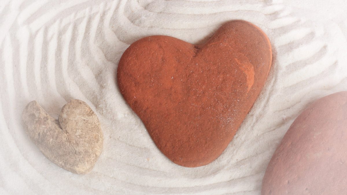 Three rough stones, each vaguely resembling the shape of a heart, in the well-groomed sand of a zen garden.