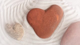 Three rough stones, each vaguely resembling the shape of a heart, in the well-groomed sand of a zen garden.