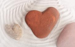 Three rough stones, each vaguely resembling the shape of a heart, in the well-groomed sand of a zen garden.