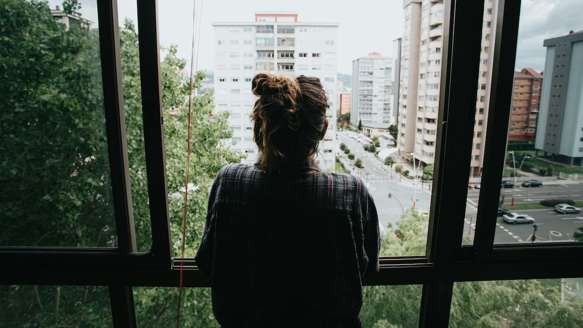a worried woman looks out the window at the surrounding city