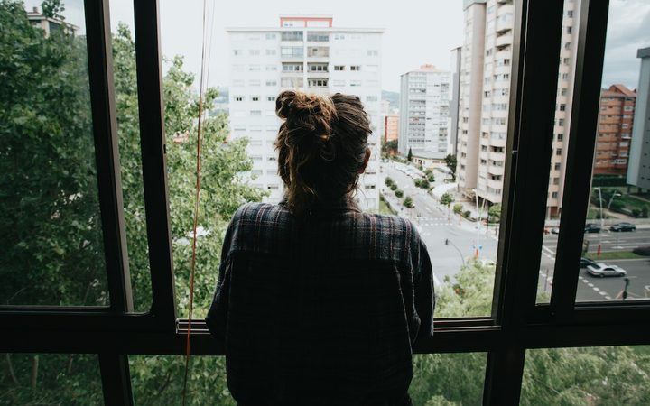 a worried woman looks out the window at the surrounding city