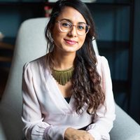 Nira Shah calmly sits in an Alma therapy space with her hands folded over her lap.