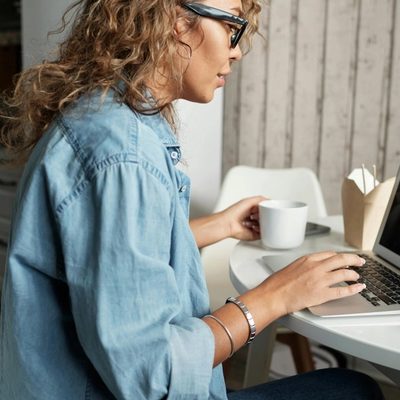 Person having a virtual meeting on their laptop while holding a cup of coffee