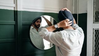 A Sikh man wearing a dastar straightens his turban in the mirror.