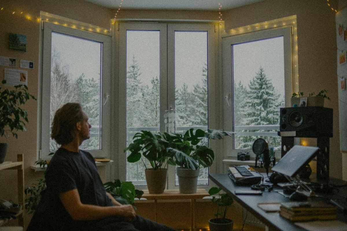 a man sitting quietly in his home office watching snow fall out his window