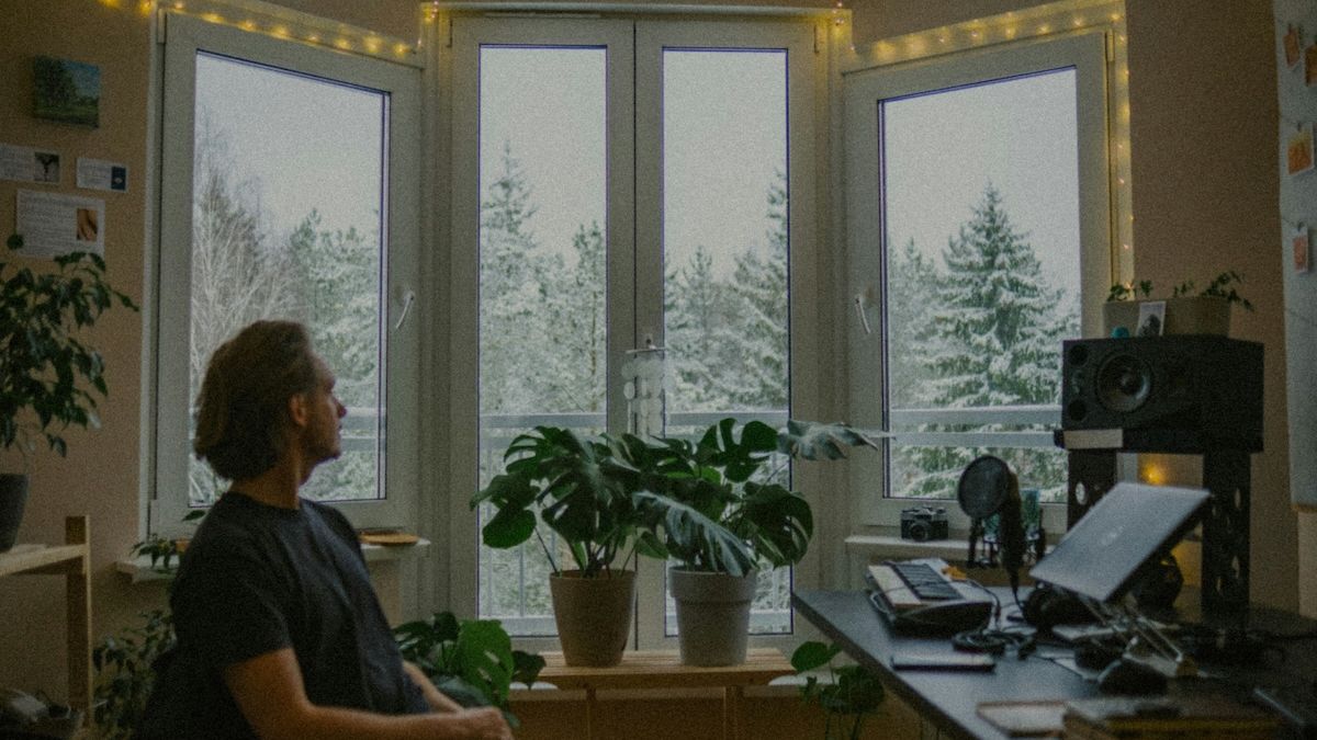 a man sitting quietly in his home office watching snow fall out his window