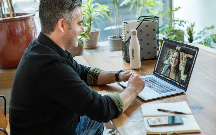 Man in black sweater using a laptop to video conference a female therapist.