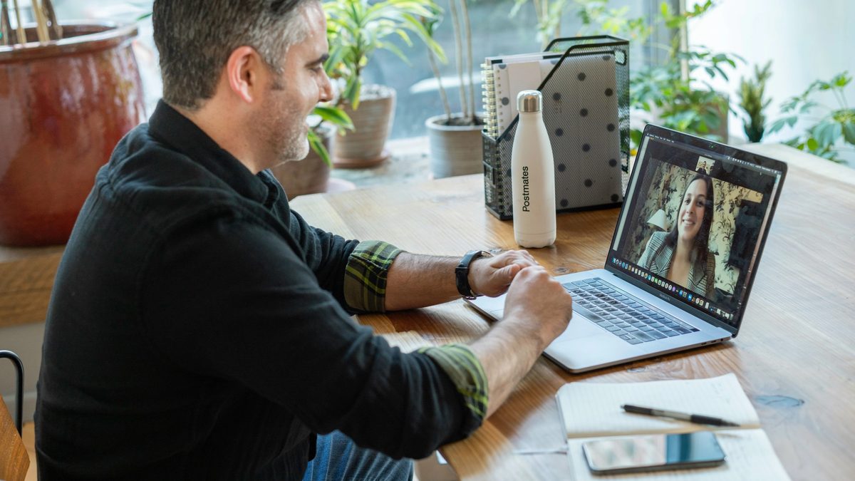 Man in black sweater using a laptop to video conference a female therapist.