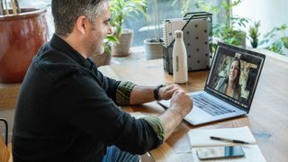 Man in black sweater using a laptop to video conference a female therapist.