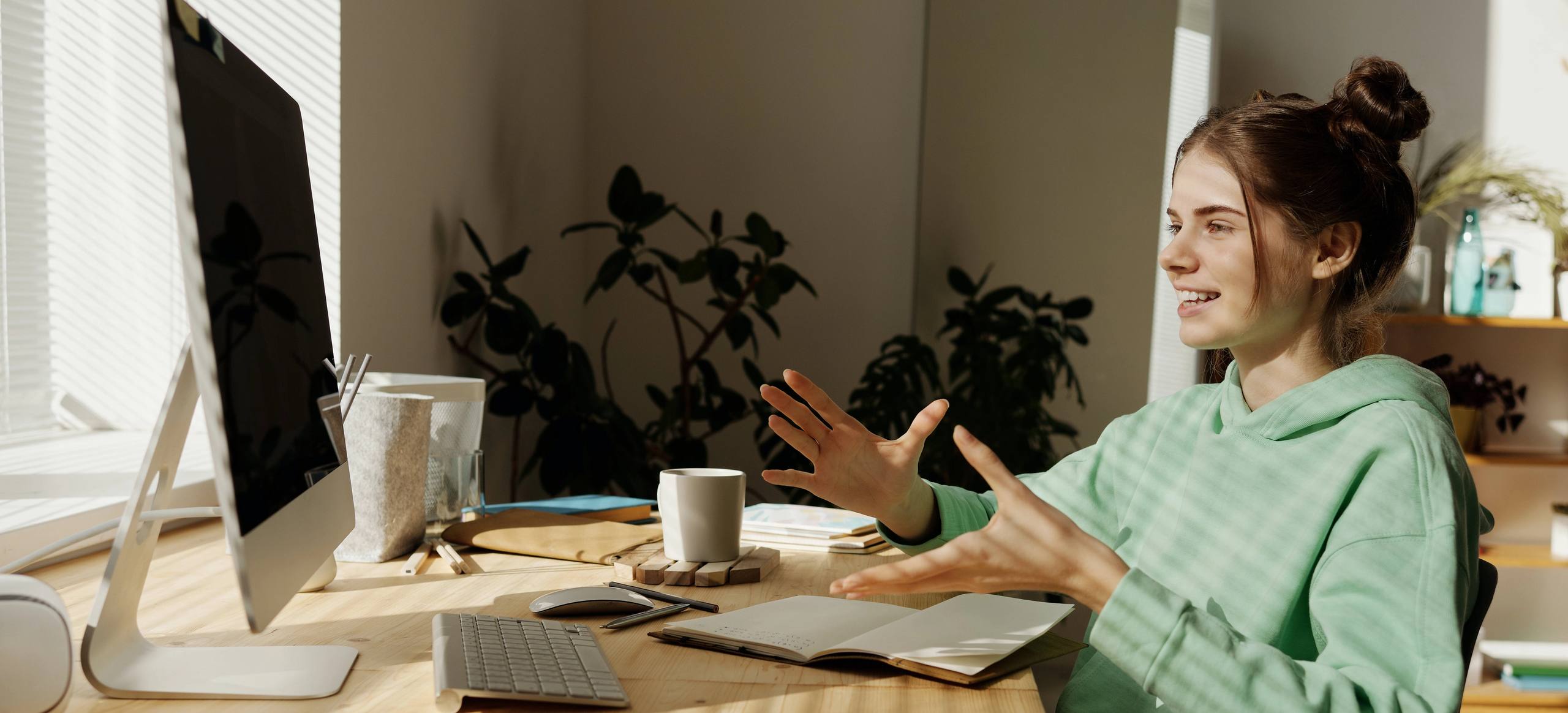 A young person at a desk at home, talking and gesturing mid-conversation