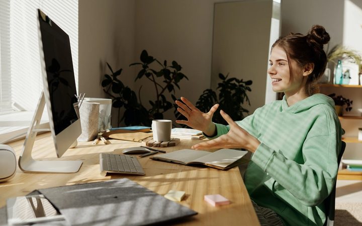 A teenager bathed in sunlight from the window, talking animatedly with her virtual therapist at her computer.