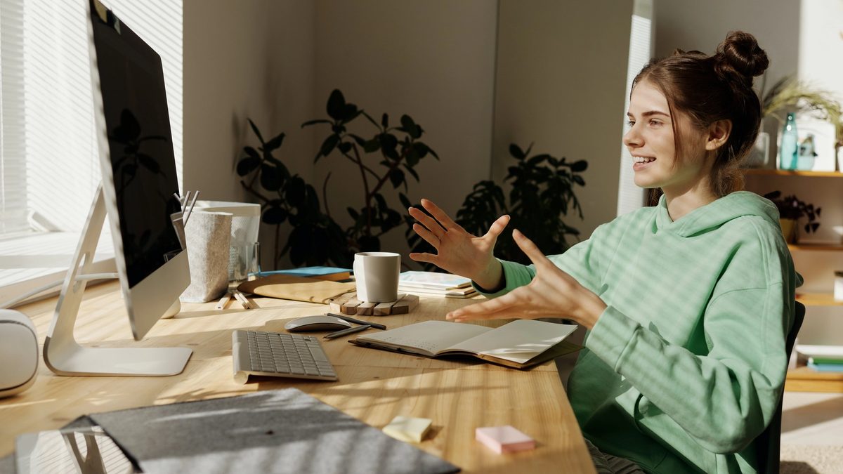 A teenager bathed in sunlight from the window, talking animatedly with her virtual therapist at her computer.